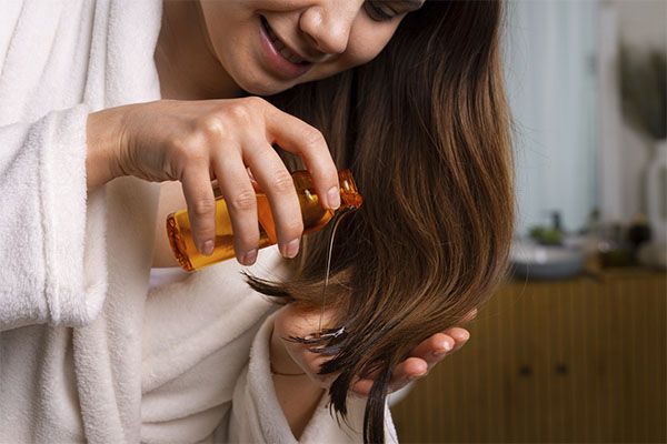 Femme mettant de l'huile capillaire sur ses cheveux bruns 
