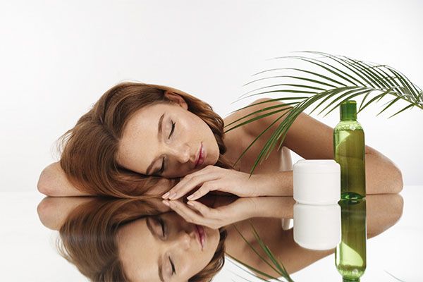 Belle femme allongée sur une table de transplantation, avec un gel et une crème pour les cheveux. Saw Palmetto pour la perte de cheveux