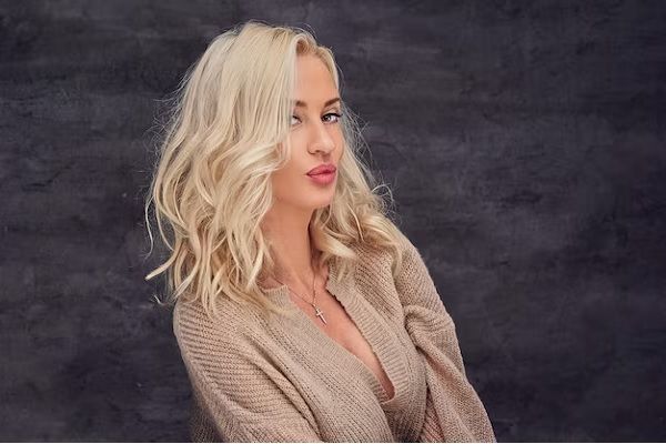 femme blonde aux cheveux bouclés sur fond gris. prendre soin des cheveux blonds 