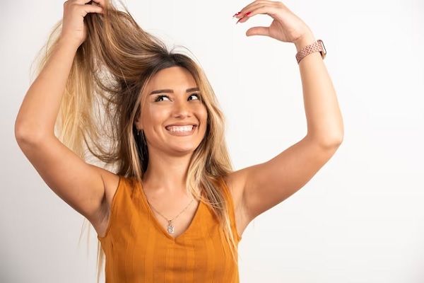 femme positive touchant ses cheveux et posant sur fond blanc