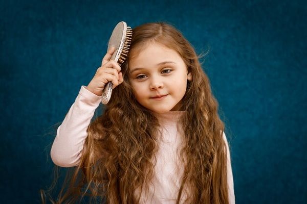 Belle enfant se brossant les cheveux blonds chic et bouclés. 