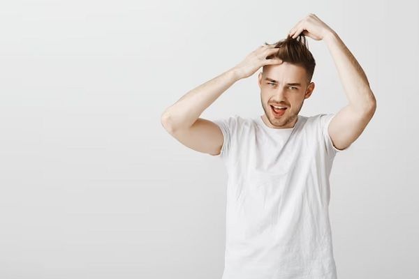 Un homme en chemise verte et au visage souriant se tient les cheveux à deux mains. 