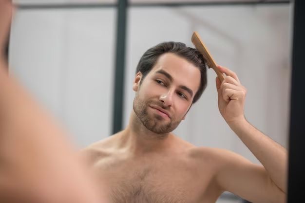 jeune bel homme se brossant les cheveux et semblant satisfait. Soins après une greffe de cheveux