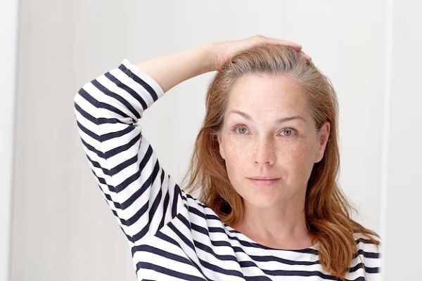 Femme souriante regardant ses cheveux gris dans un miroir et se reflétant sur une racine de croissance. SOPK perte de cheveux