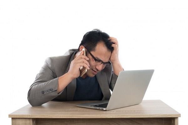 homme inquiet assis devant un ordinateur portable et parlant au téléphone. le stress influence-t-il la chute des cheveux
