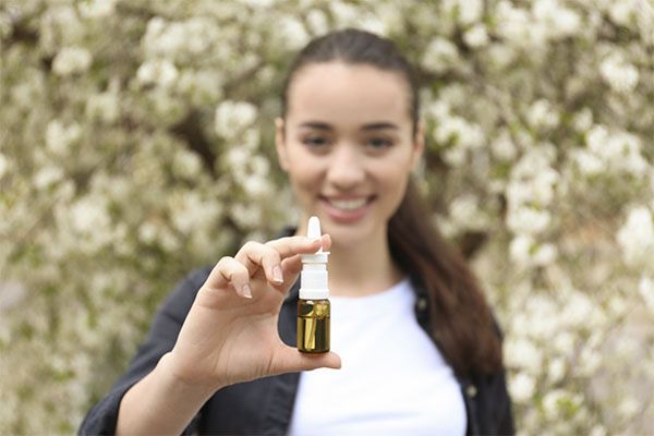Jeune femme avec gouttes nasales près d'un arbre en fleurs. l'huile de babassu pour les cheveux