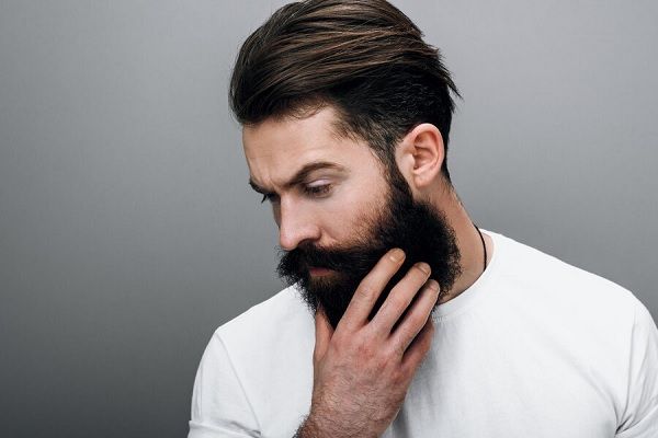 Homme barbu en chemise blanche, la main sur le visage.