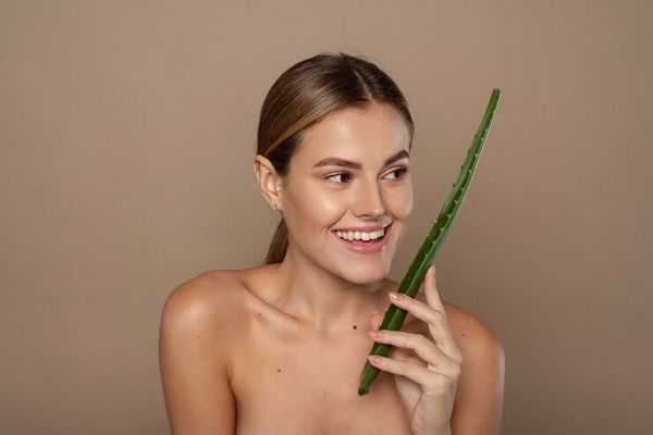 Souriante jeune femme heureuse tenant une feuille d'aloès dans ses mains sur beige