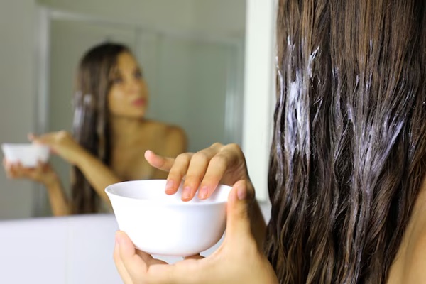 Belle femme appliquant un produit capillaire en se regardant dans un miroir. 
