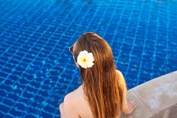 Dos de la femme caucasienne aux cheveux longs et aux fleurs assise au bord de la piscine