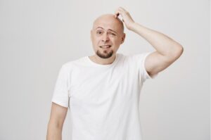 Un homme chauve d'âge moyen se gratte la tête, perplexe.