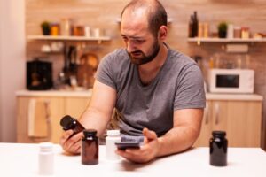 Homme souffrant de maux de tête et tenant un flacon de pilules, assis dans la cuisine. 