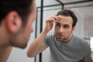  Un jeune homme vêtu d'un tee-shirt gris se regarde dans le miroir.