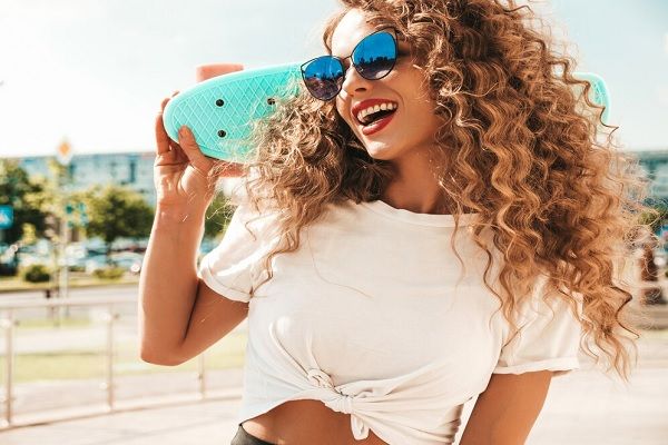 Fille avec penny skate bleu posant dans la rue. Les soins des cheveux en été 