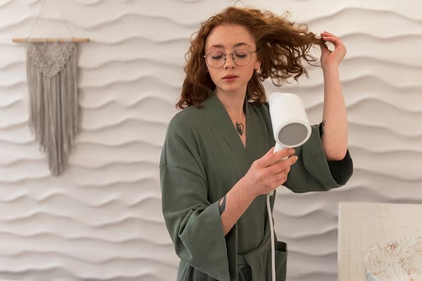 Femme utilisant un sèche-cheveux pendant sa routine beauté. erreurs à éviter routine soins capillaires