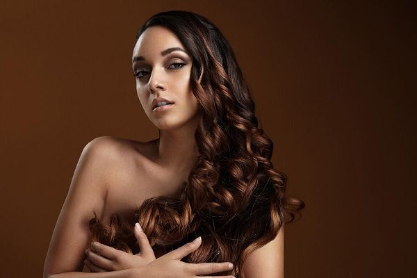 Fille tenant ses cheveux bouclés. Comment avoir des cheveux brillants et soyeux naturellement