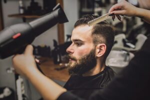 Femme en coupe séchant les cheveux d'un homme dans un salon de coiffure