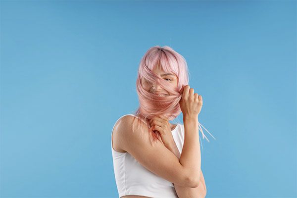 Belle femme aux cheveux roses décolorés et à la chemise blanche, se tenant les cheveux en croix. 
