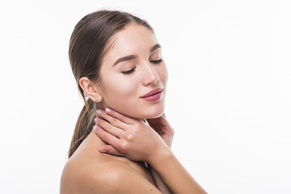 Quels sont les soins esthétiques les plus pratiqués en France? une belle femme aux cheveux bruns porte les deux mains à son cou 