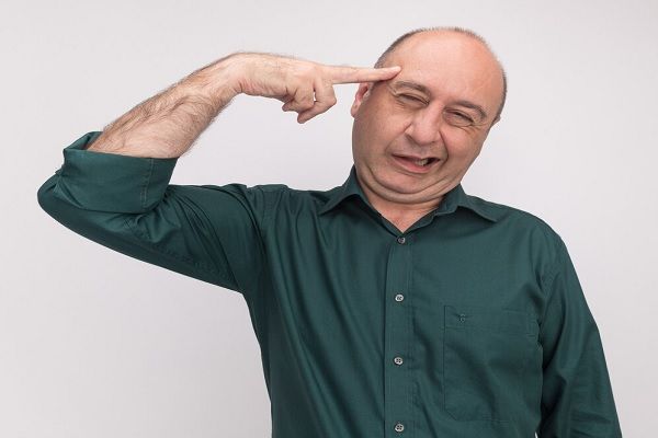 Joyeux homme d'âge moyen en t-shirt vert mettant le doigt sur le temple isolé sur un mur blanc. Quelle est la relation entre la greffe de cheveux et le bonheur