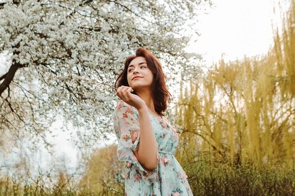 Portrait d'une charmante femme posant près de fleurs de cerisier en fleurs dans le jardin. Comment prendre soin de ses cheveux au printemps 