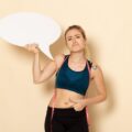 Vue de face d'une jeune femme en tenue de sport tenant un panneau blanc et mesurant son corps sur un mur blanc clair. Santé du corps, sport, beauté, exercice, forme. Comment améliorer votre santé digestive Conseils et aides
