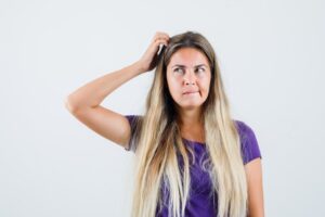 Femme blonde se grattant la tête en t-shirt violet, l'air pensif, vue de face.
