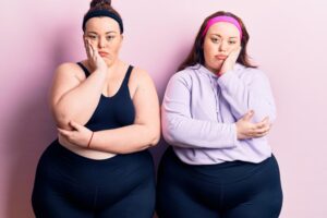 Jeunes jumelles de grande taille portant des vêtements de sport et ayant l'air fatiguées et ennuyées avec des problèmes de dépression, les bras croisés.